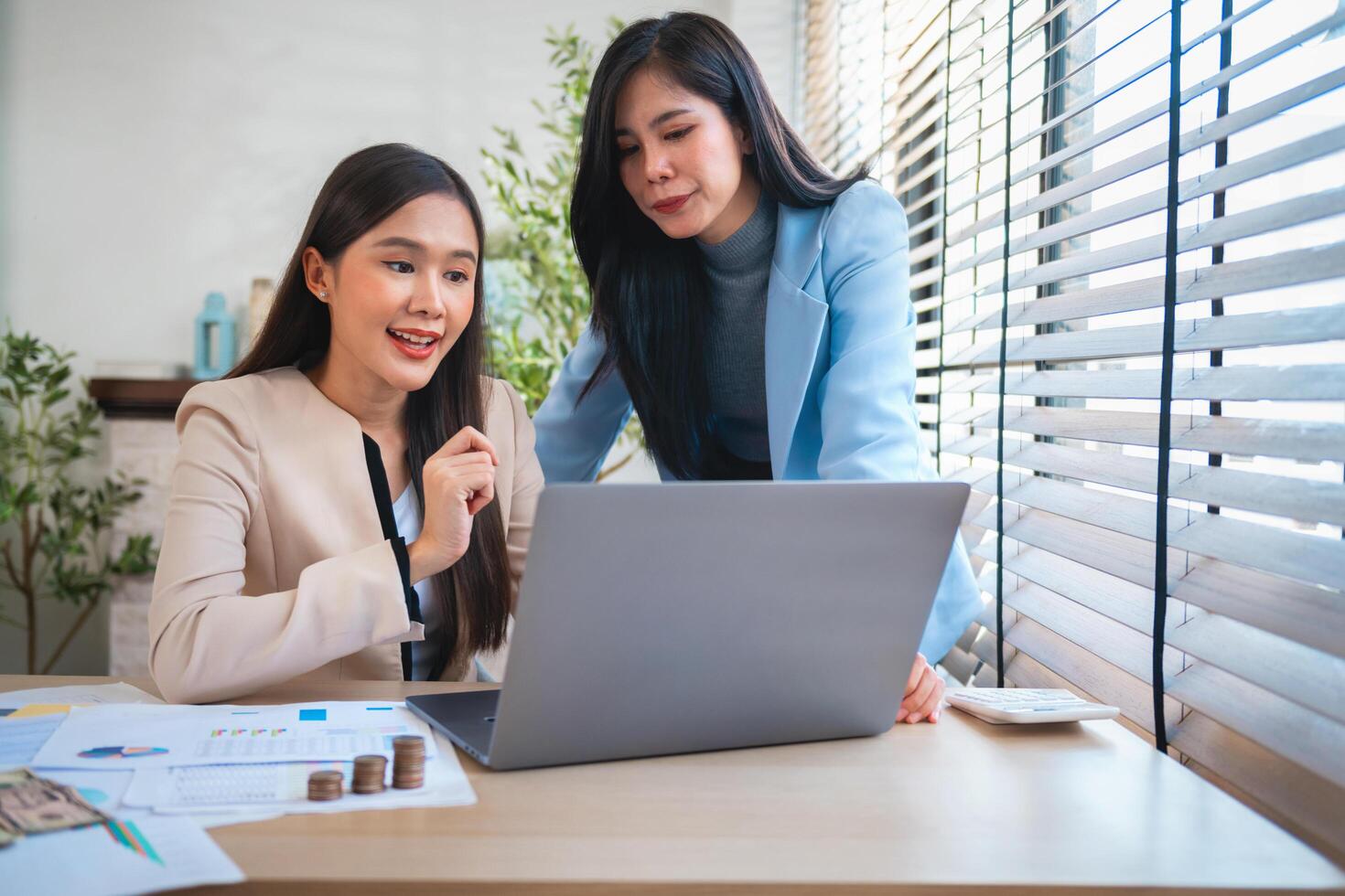Two women are sitting at a desk with a laptop open in front of them photo