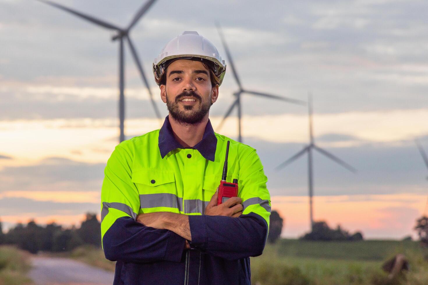 man in a yellow and blue safety vest stands in front of a wind farm photo