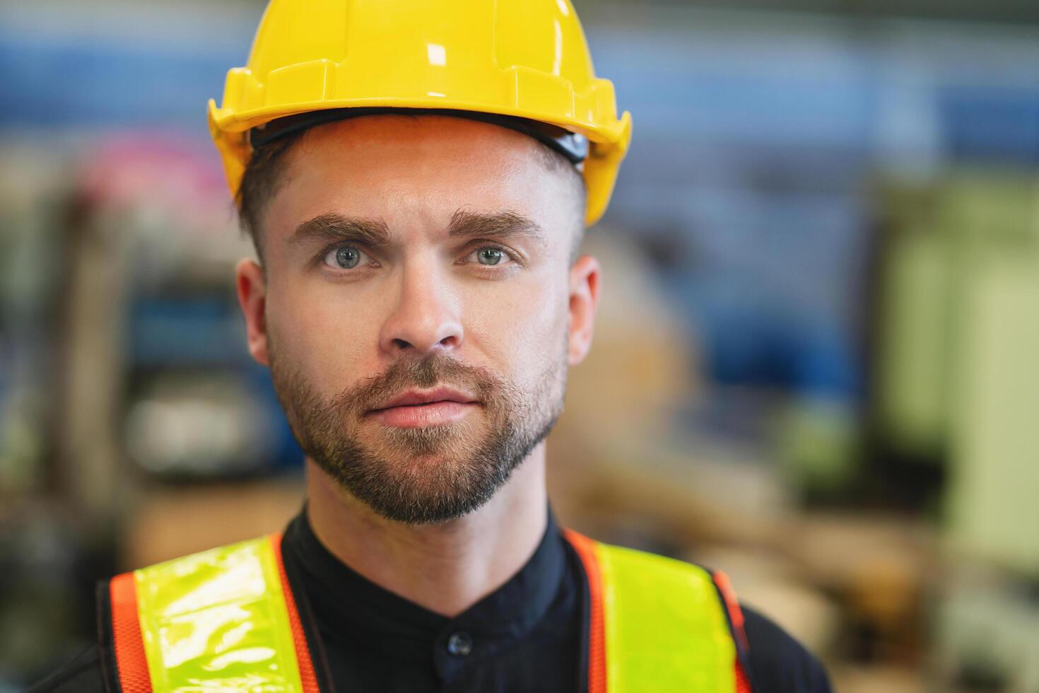 man wearing a yellow hard hat and a reflective vest is standing in a factory photo