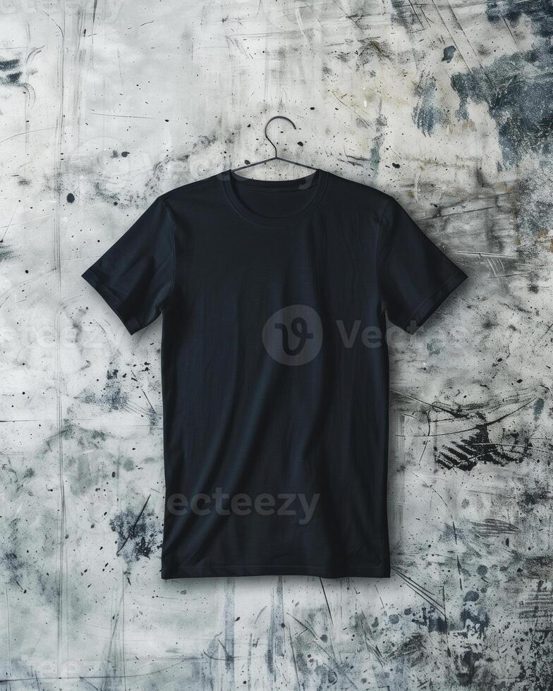 A plain black t-shirt is laid flat on a textured, grungy concrete background, showcasing its simple design and fabric texture. photo