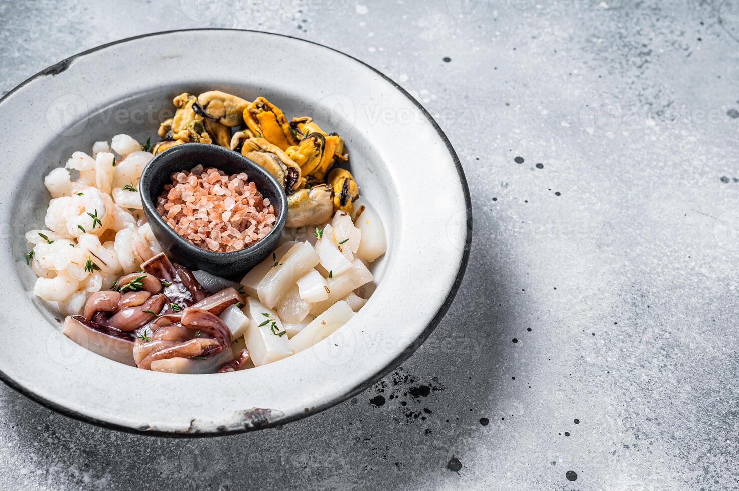 Raw seafood mix in a rustic plate. Gray background. Top view. Copy space photo