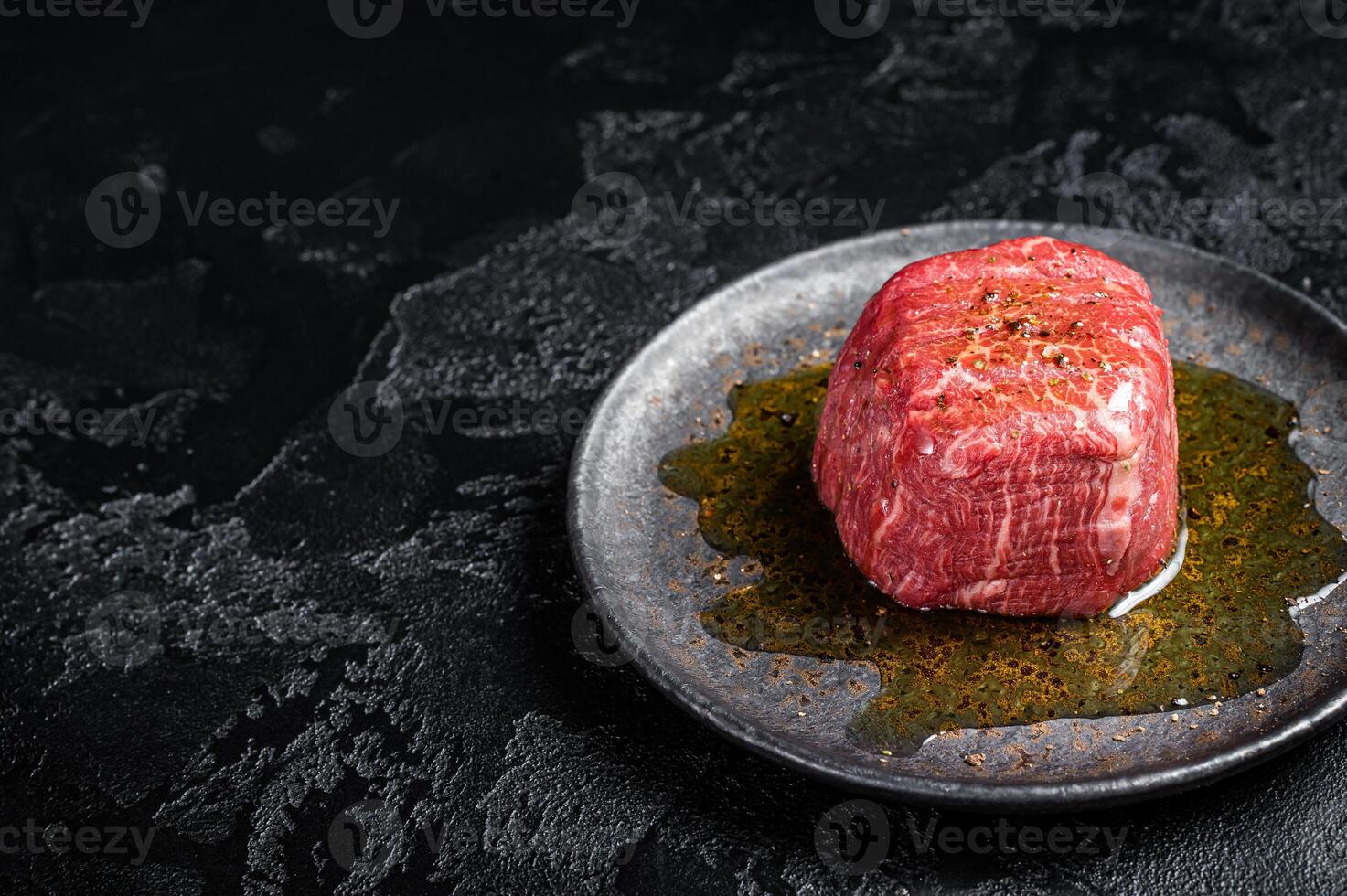 Fillet Mignon prime beef steak, raw dry aged marble meat with herbs and spices ready for cooking. Black background. Top view. Space for text photo