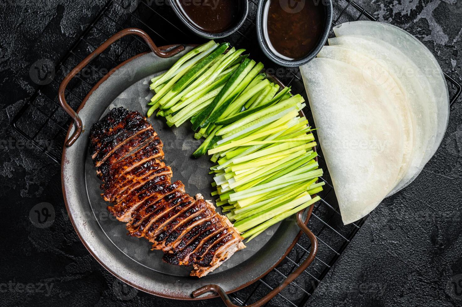Peking Duck served with cucumber, green onions, and roasted wheaten chinese pancakes with sauce Hoysin. Black background. Top view photo