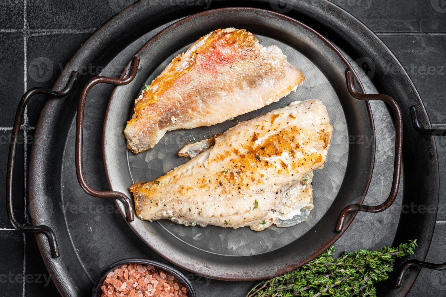 Roasted ocean red perch fillet with olive oil, thyme and spices. Black background. Top view photo