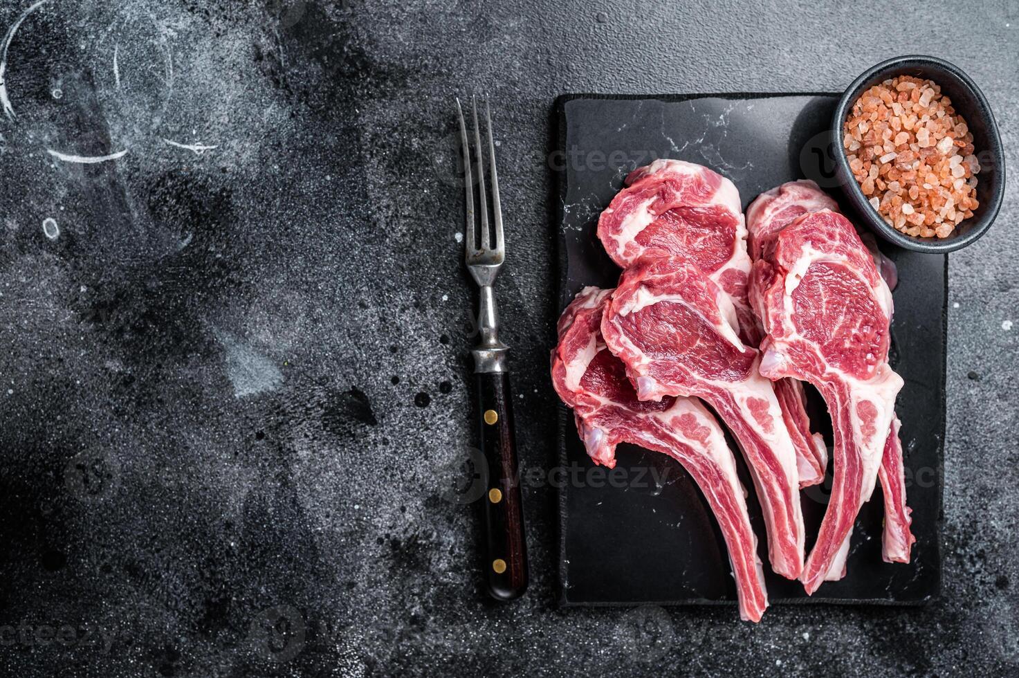 Uncooked lamb mutton chops, raw meat steaks. Black background. Top view. Copy space photo