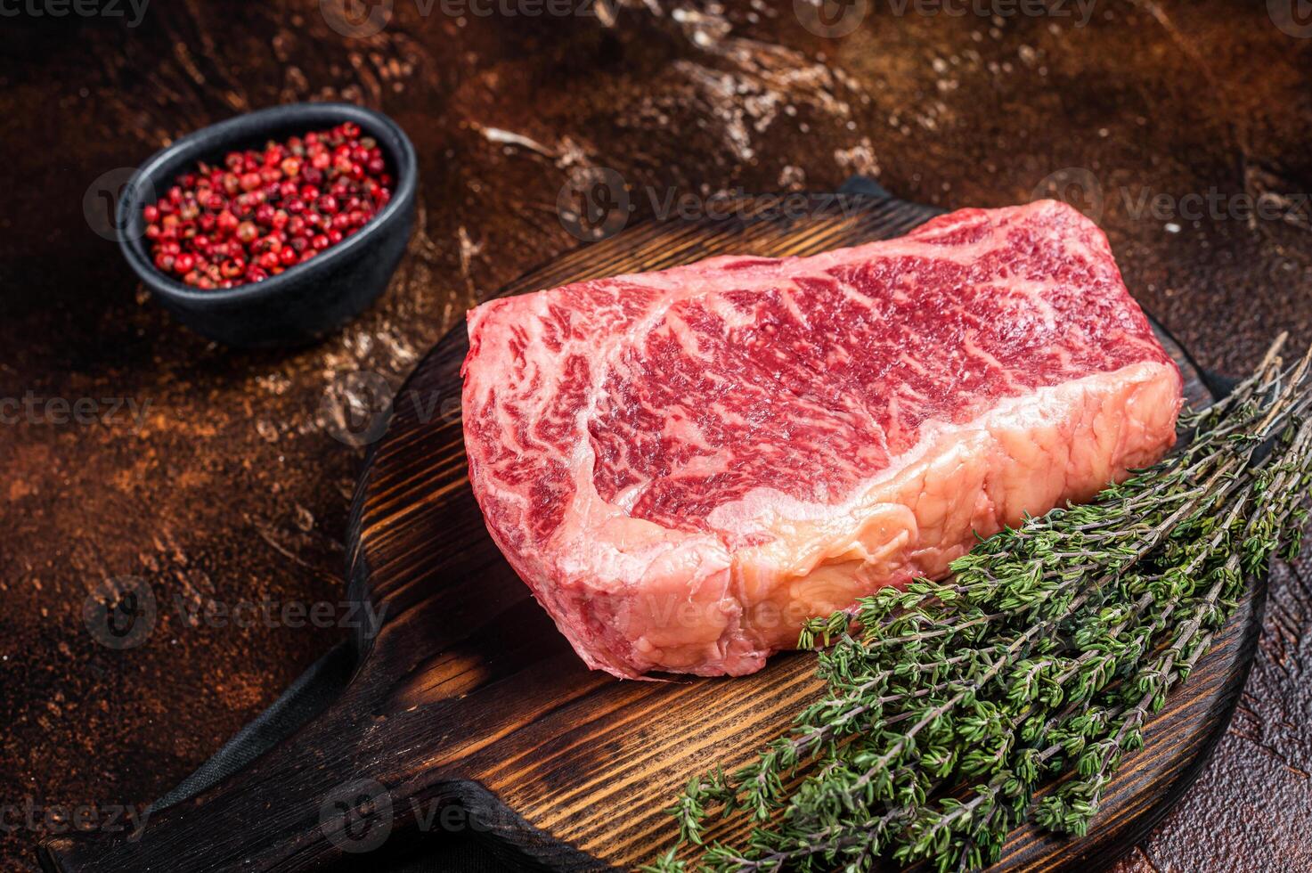 Uncooked Raw striploin or club steak on wooden board with thyme. Dark background. Top view photo