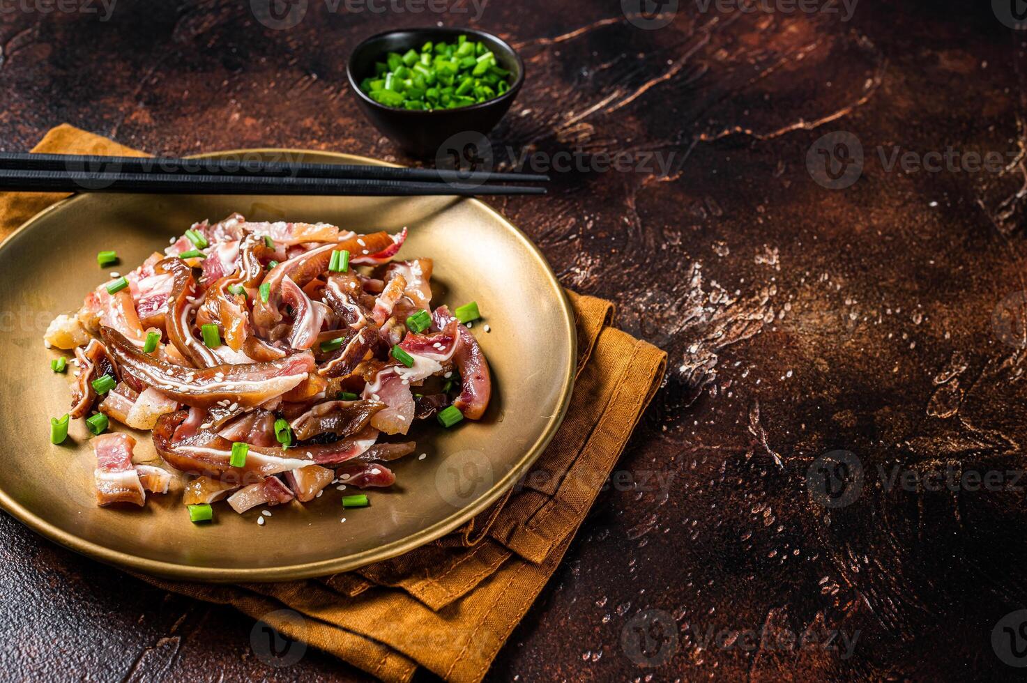 Asian appetizer pig pork ears with sesame seeds, green onion and spicy sauce. Dark background. Top view. Copy space photo
