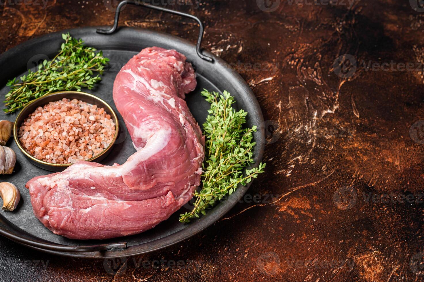 Uncooked Raw pork tenderloin fillet meat on a kitchet tray with thyme, garlic and sea salt. Dark background. Top view. Copy space photo
