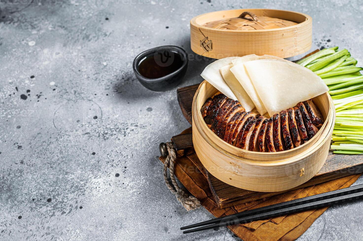 Peking Duck in bamboo steamer served with cucumber, green onion, and wheaten chinese pancakes and sauce Hoysin. Gray background. Top view. Copy space photo