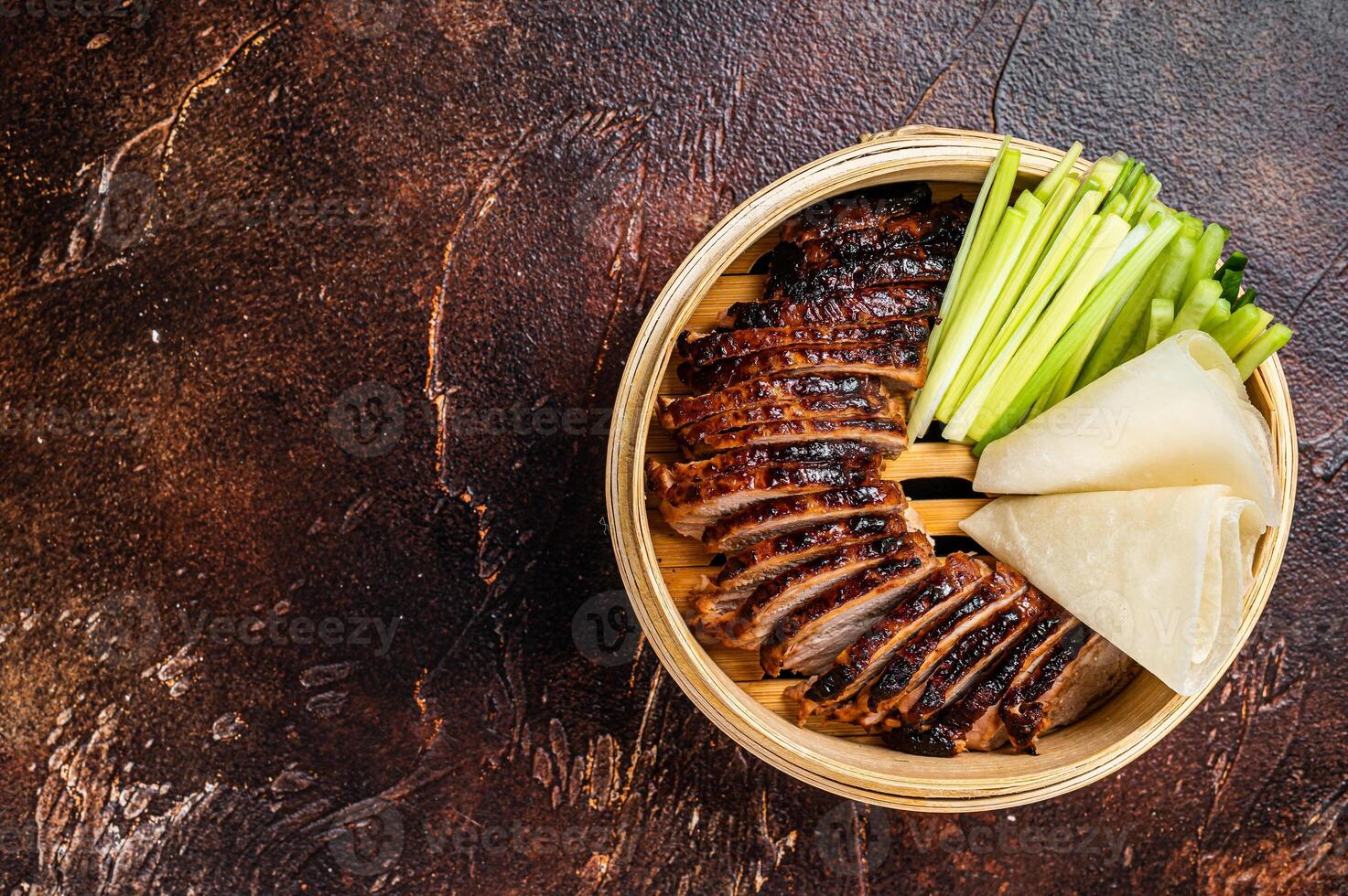 Peking Duck in bamboo steamer served with cucumber, green onion, and wheaten chinese pancakes. Dark background. Top view. Copy space photo