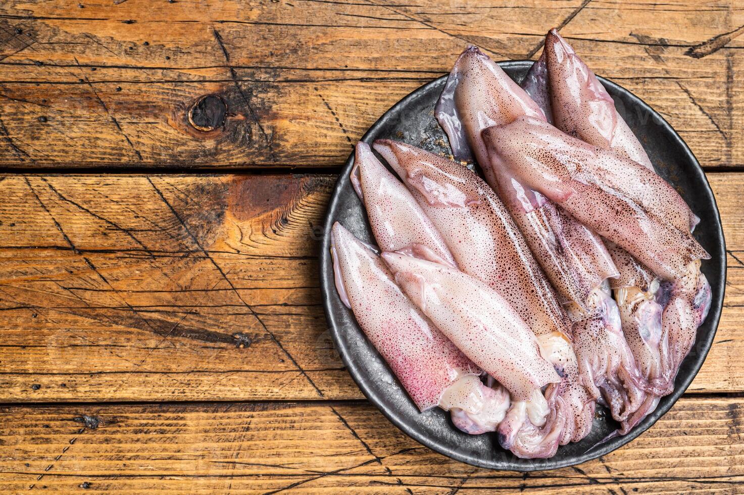 Raw squid, fresh calamari in a plate. Wooden background. Top view. Copy space photo