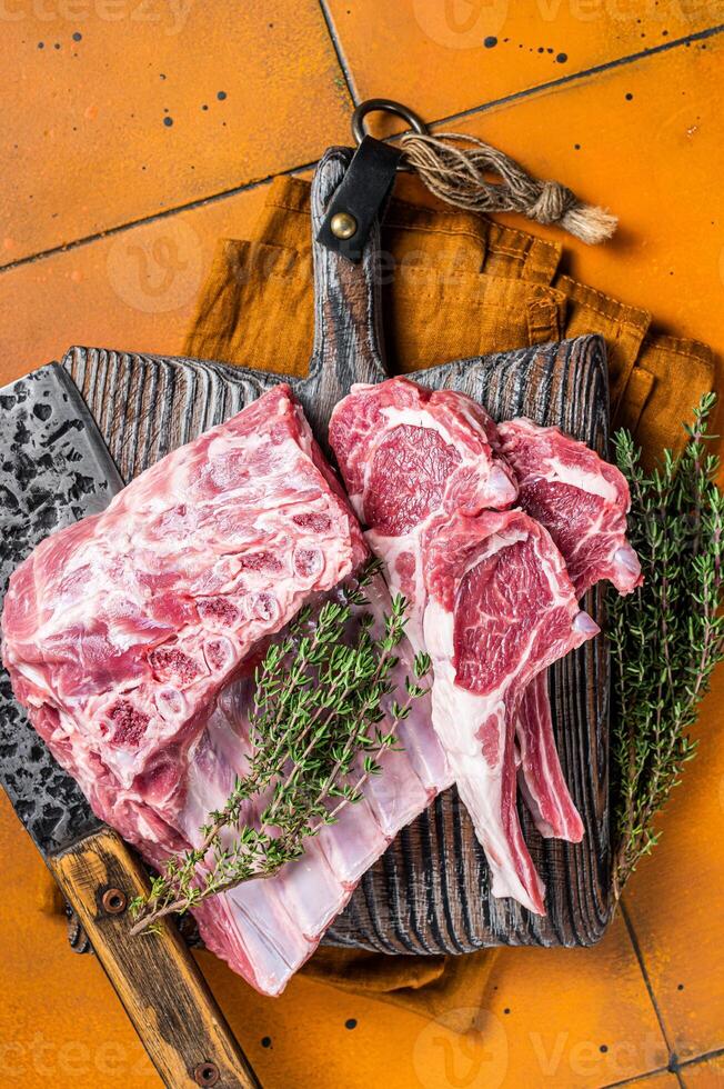 Raw lamb meat chops cutlets on butcher cutting board. Orange background. Top view photo