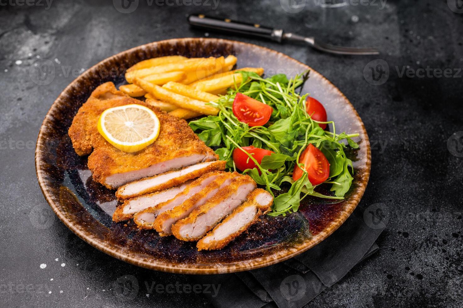 Roast viennese schnitzel steak, breaded meat with salad and french fry on a plate. black background. top view photo