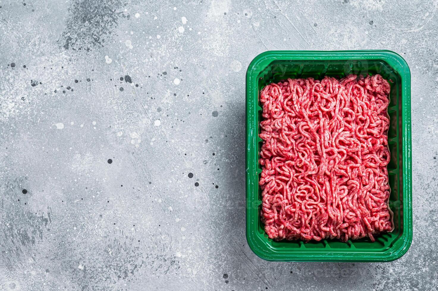 Raw Minced Meat in a Plastic Container, ground beef. Gray background. Top view. Space for text photo