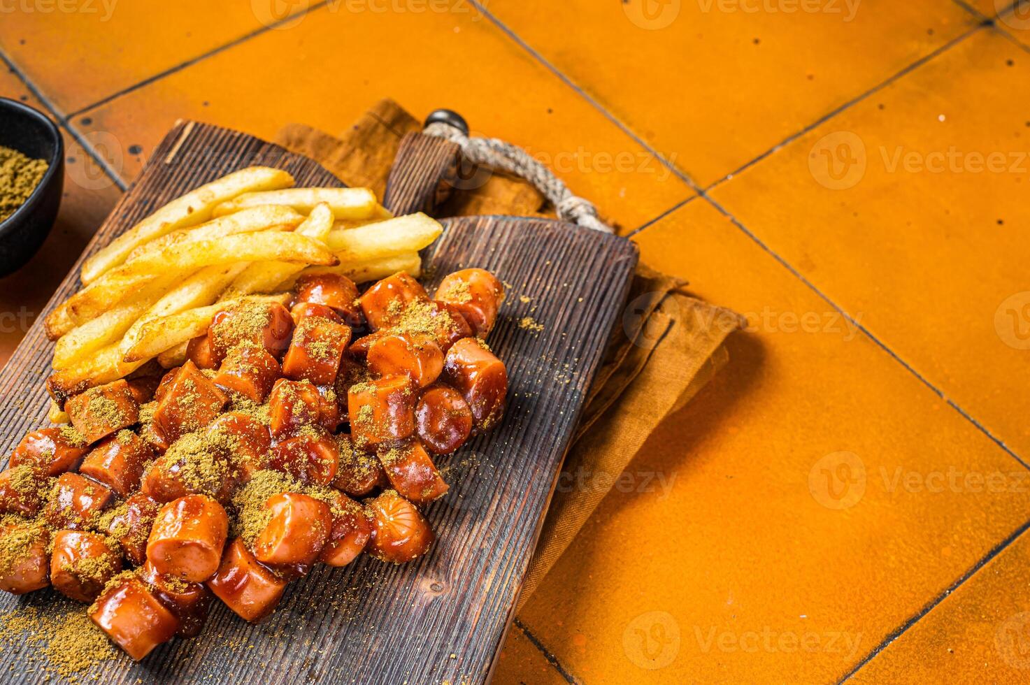 Curried sausage currywurst meal, curry wurst with french fry served on a wooden board. Orange background. Top view. Copy space photo