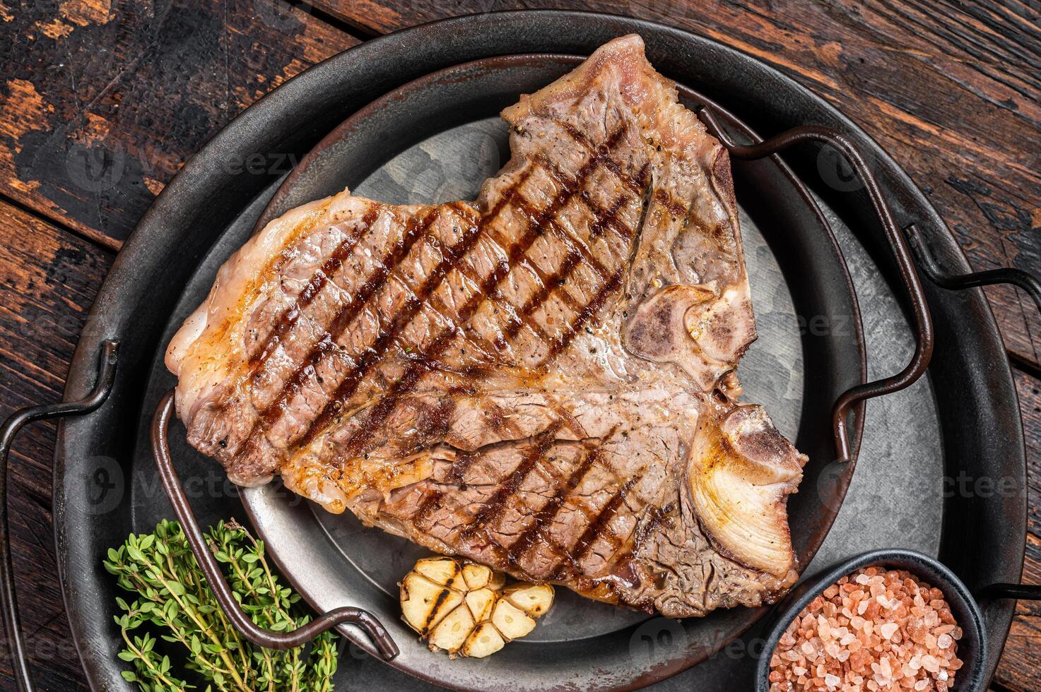 BBQ Grilled T-bone or Porterhouse beef meat Steak on a steel tray with herbs. Wooden background. Top view photo