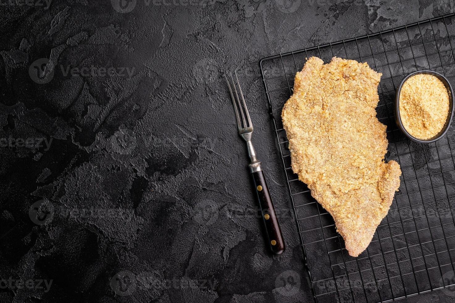 Raw breaded pork Schnitzel steak on a rack. black background. top view photo