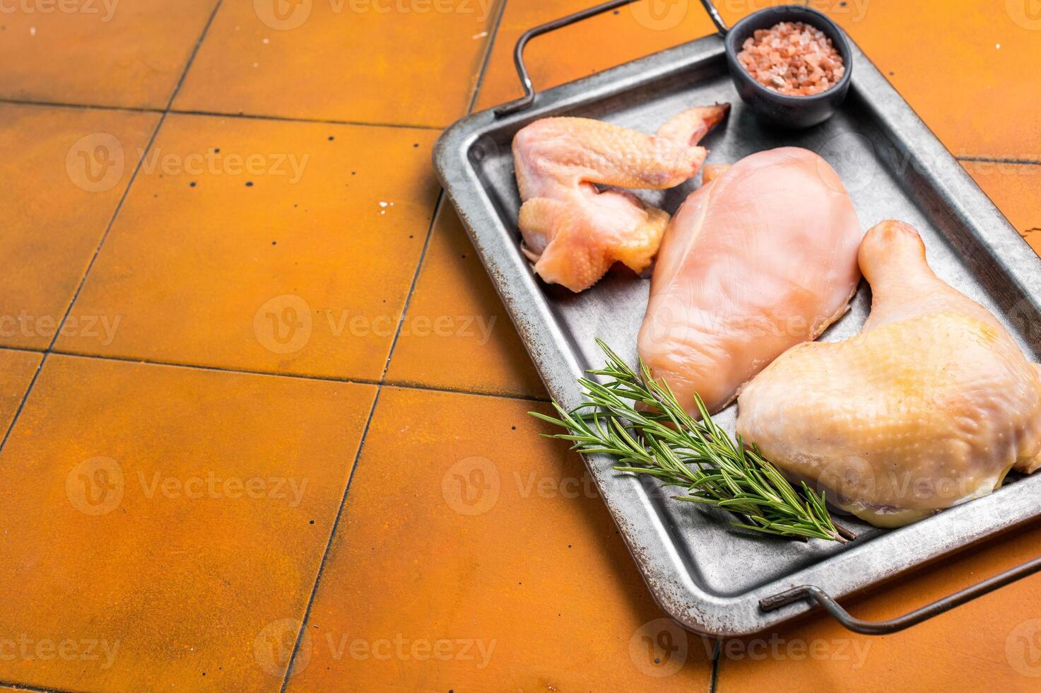 Raw chicken pieces on a metal tray with rosemary photo