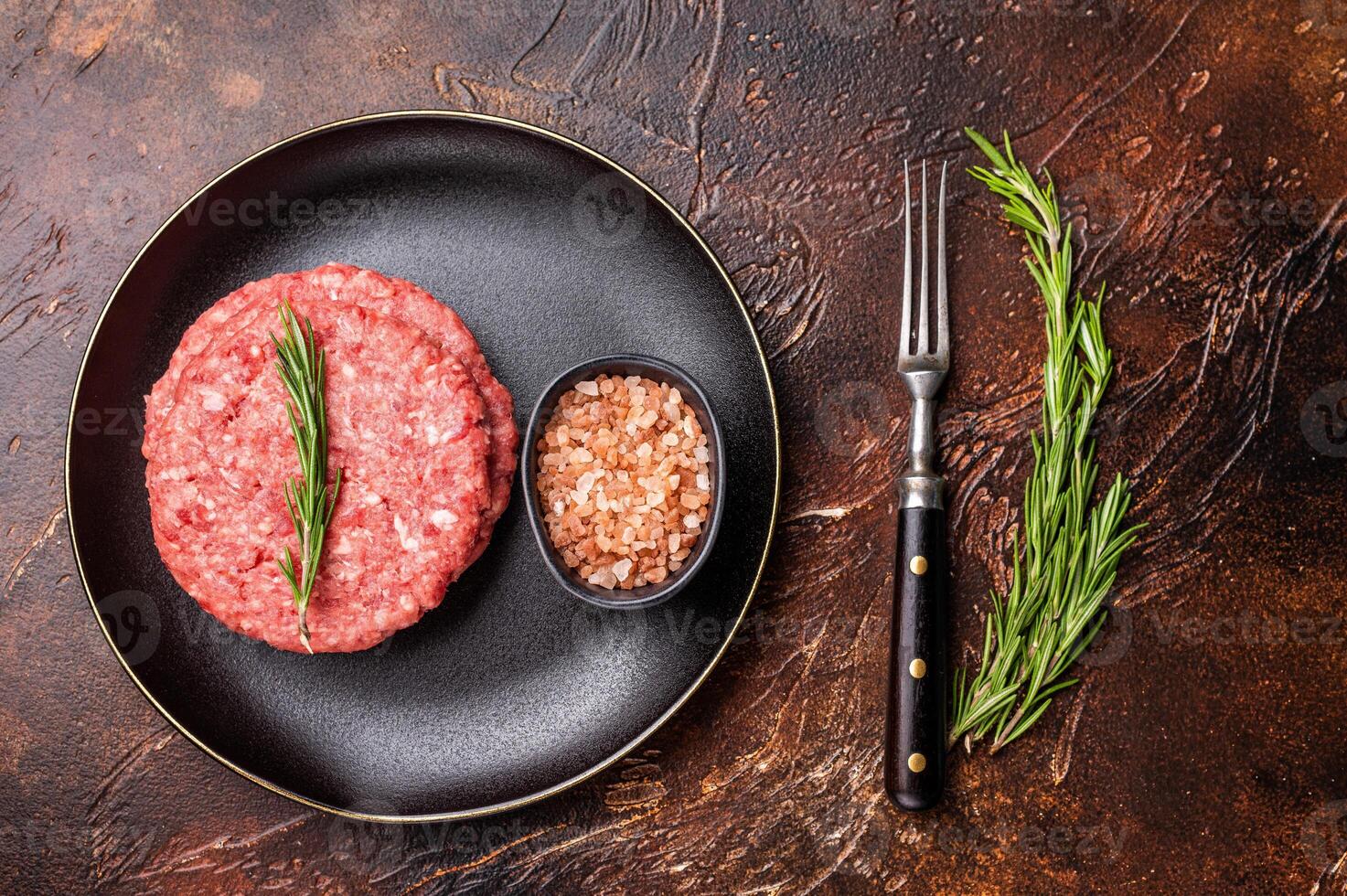 Raw veal and beef minced meat cutlets for burgers with herbs on plate. brown background. top view photo