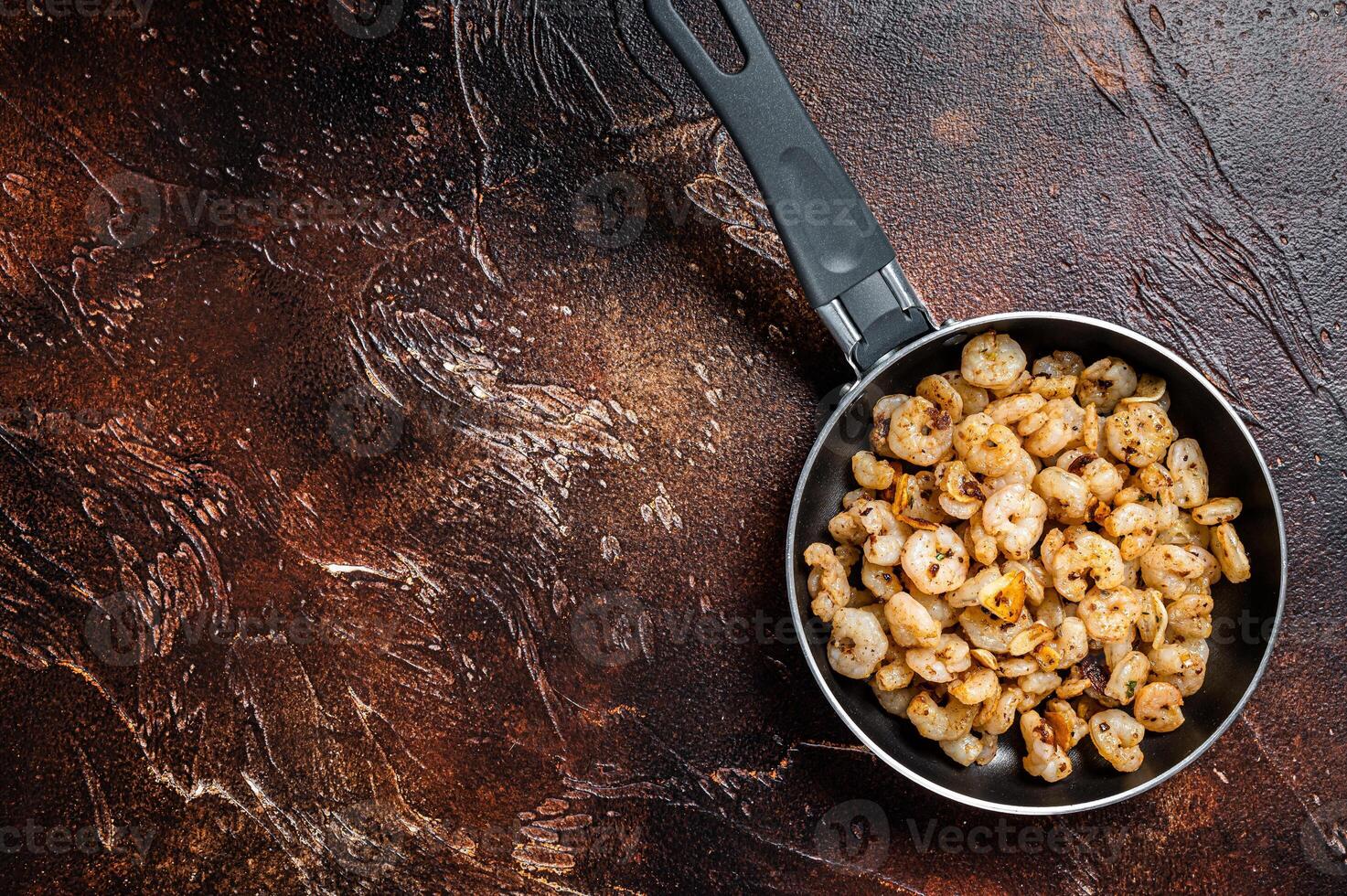 Fried peeled Shrimps prawns with garlic, olive oil in a skillet. Dark background. top view. copy space photo