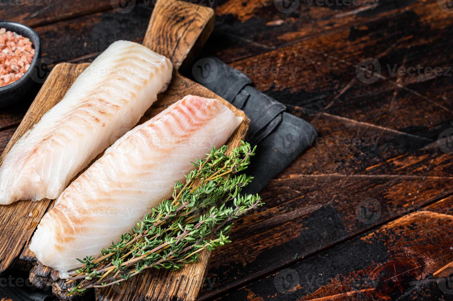 Cod fish fillets, raw codfish with thyme on wooden board. Wooden background. Top view. Copy space photo