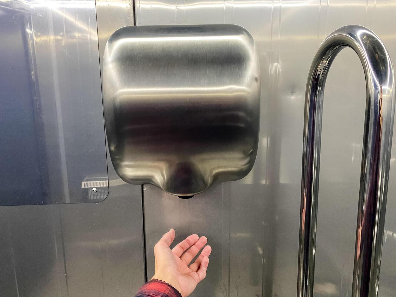 The Modern Stainless Steel Hand Dryer in a Public Restroom is designed for convenience, featuring an outstretched hand for easy use photo