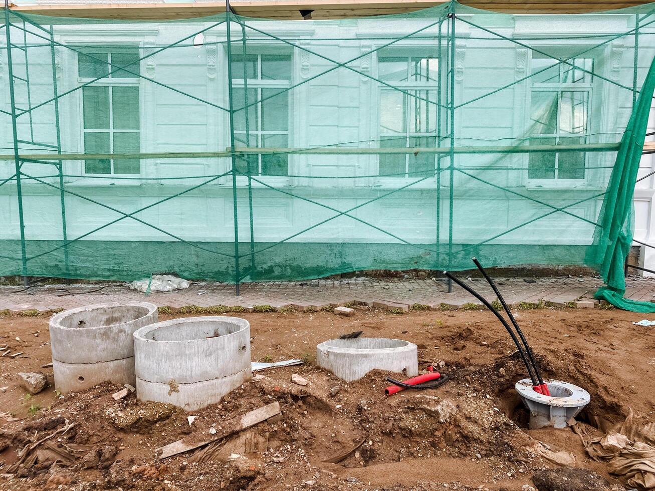 A construction site featuring scaffolding and concrete rings embedded in the earth, surrounded by various materials and elements related to building and landscaping activities photo