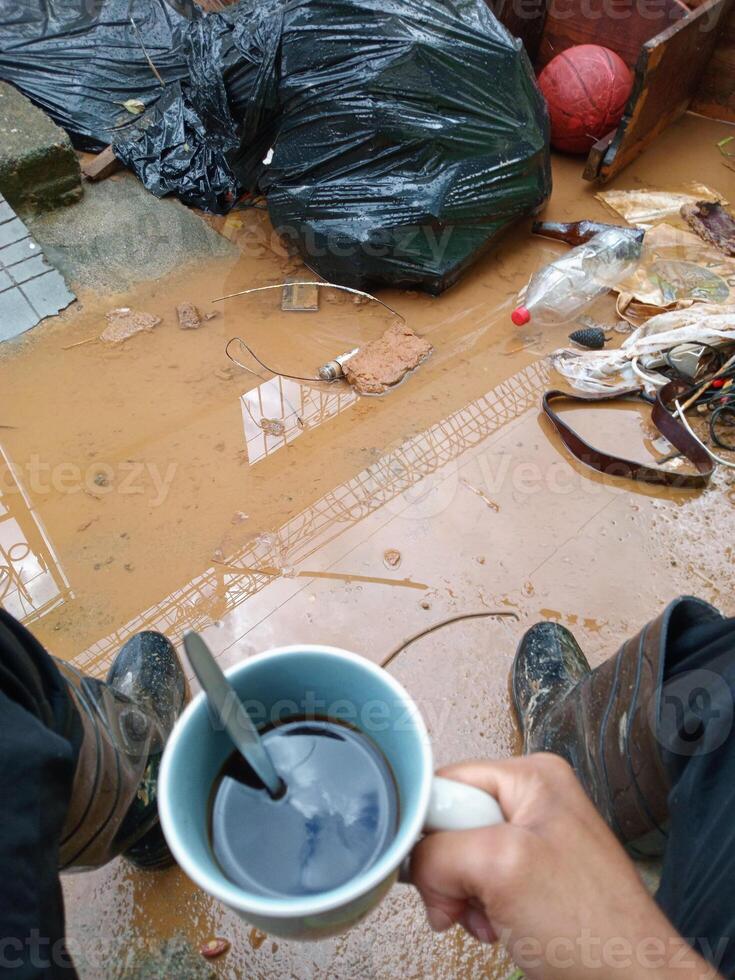 POV of hands of person holding a coffee cup front a inundation with mud and garbage. photo
