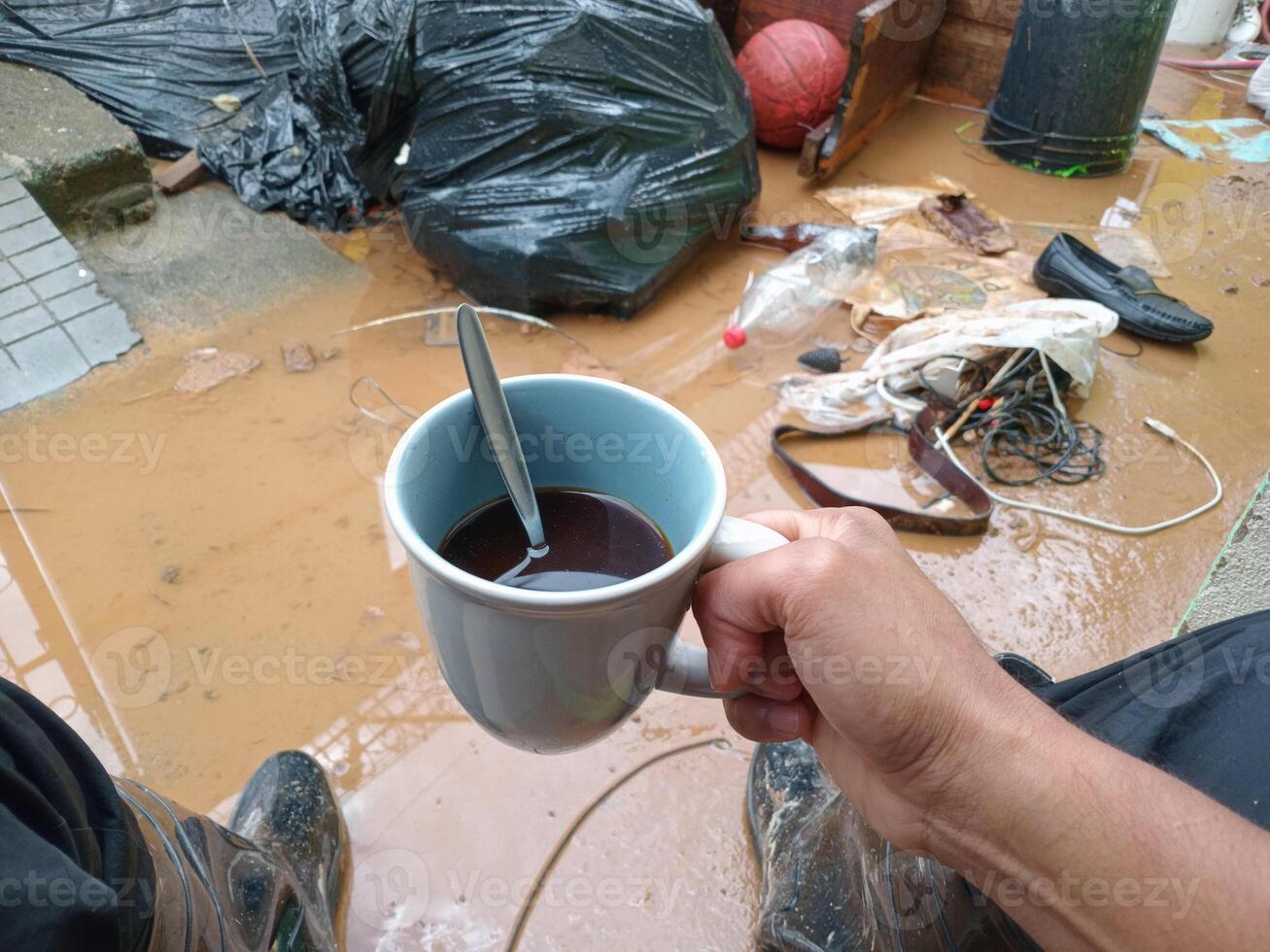 POV of hands of person holding a coffee cup front a inundation with mud and garbage. photo