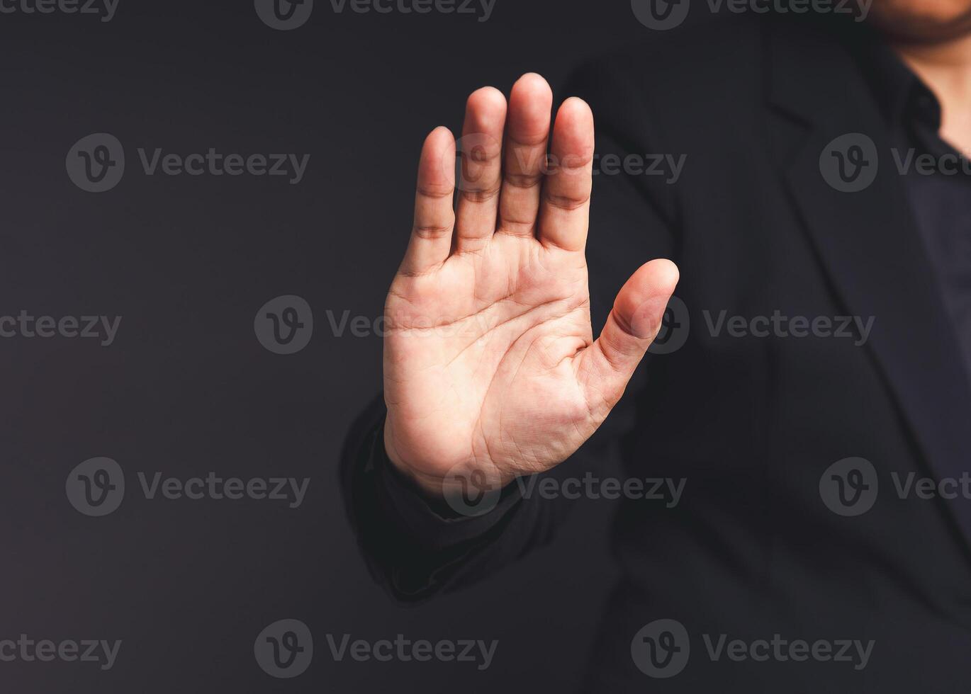 A businessman in a black suit shows a stop gesture while standing on a black background photo