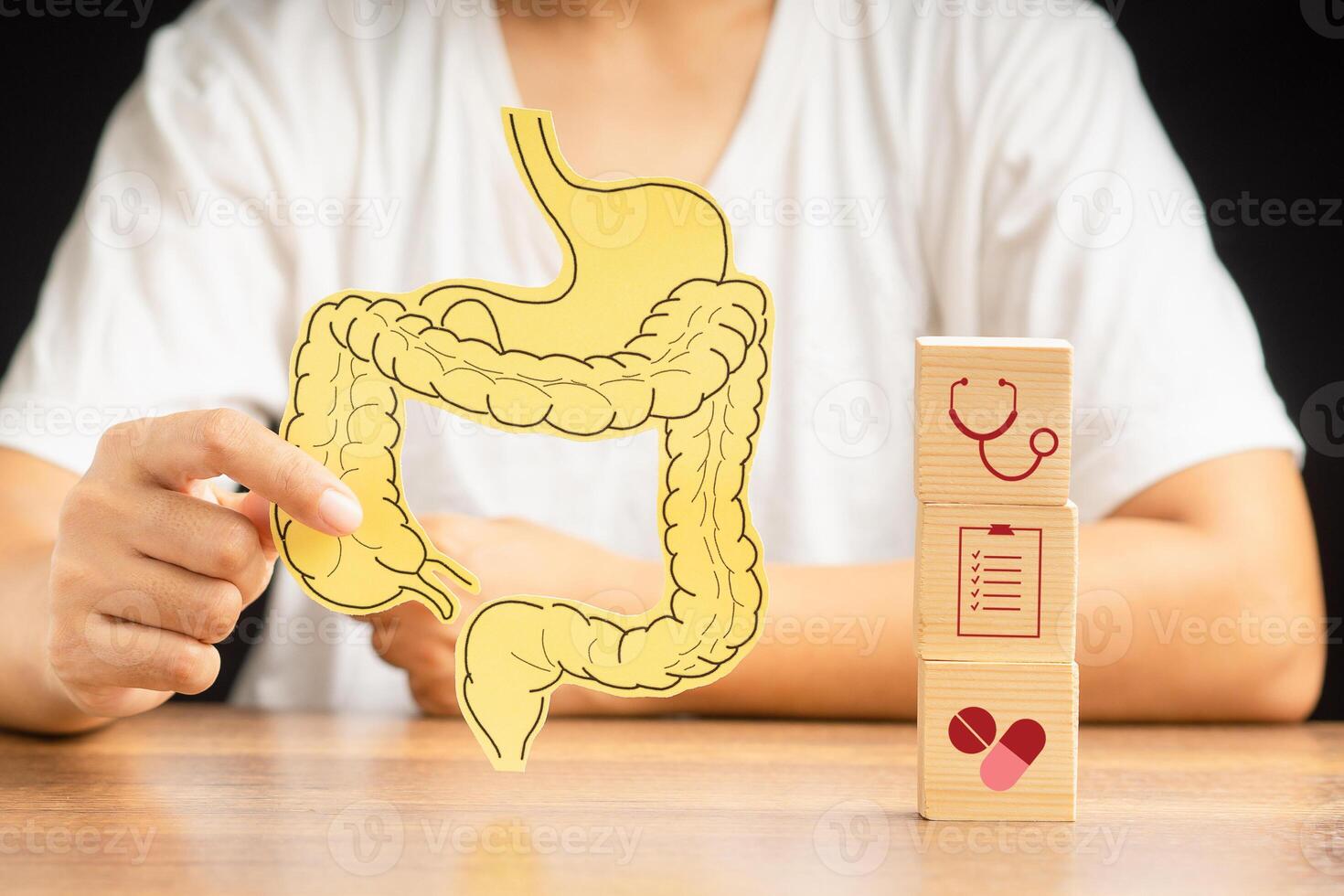 Hand holding a large intestine shape made from yellow paper and wooden cubes with health icons on the table. photo