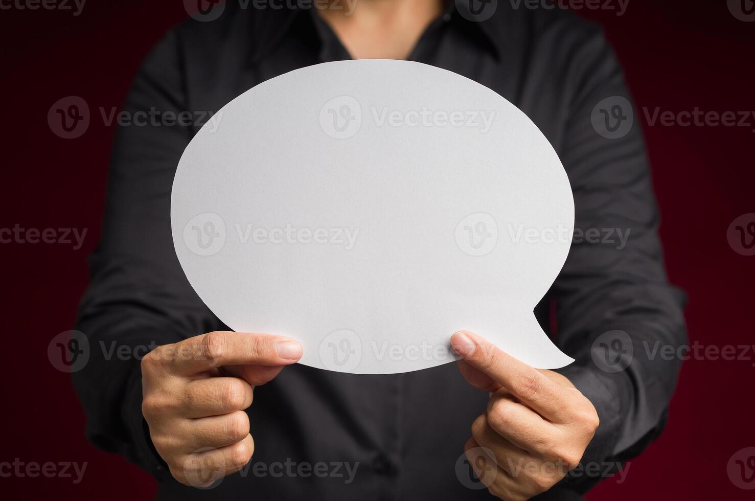Text speech bubble concept. Close-up of hand holding a white speech bubble against a red background photo