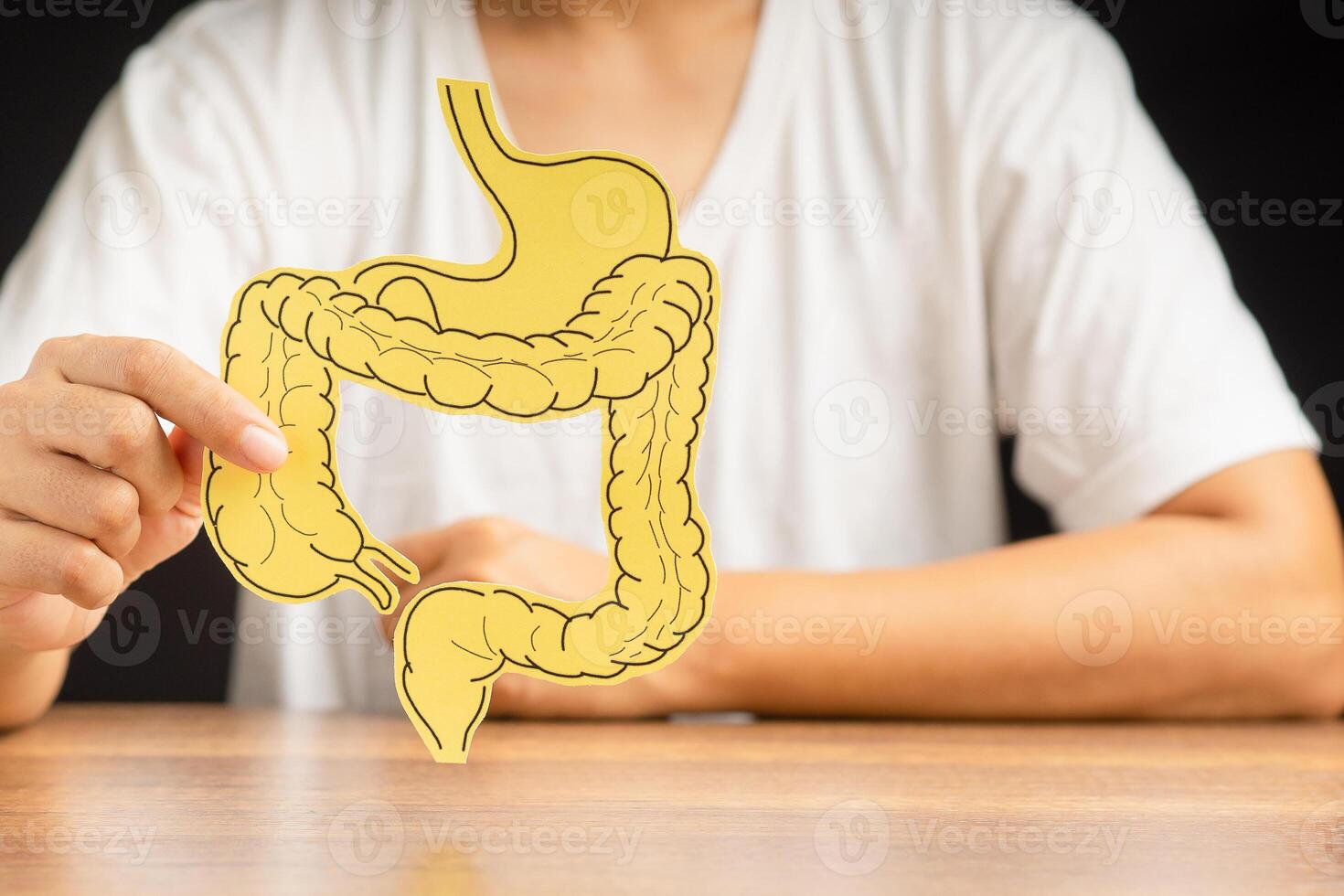 Hand holding a large intestine shape made from paper while sitting over a black background photo