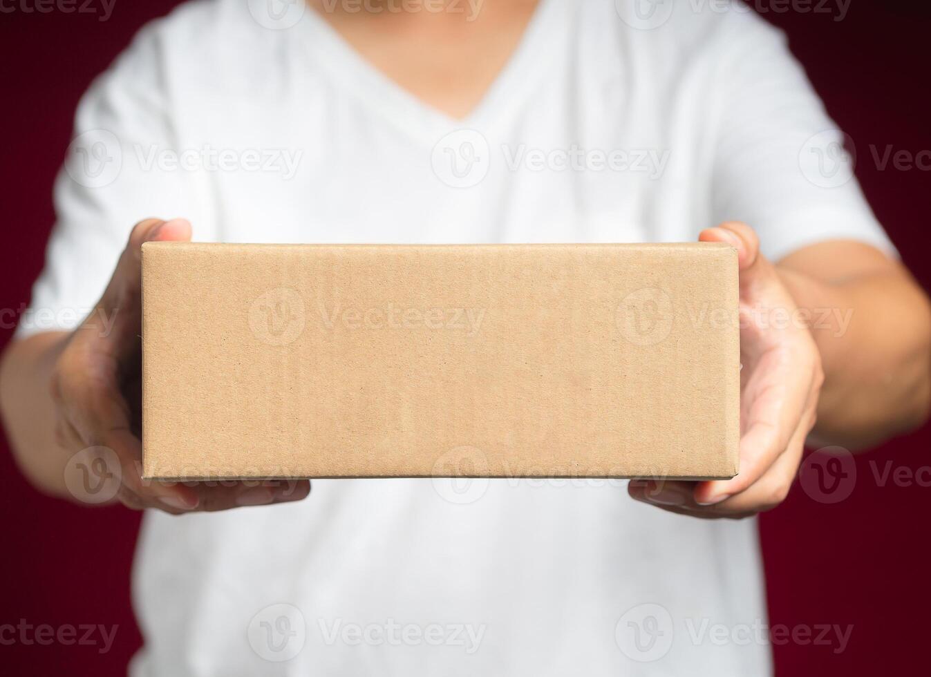 Man in white casual holding a cardboard box while standing on a red background photo