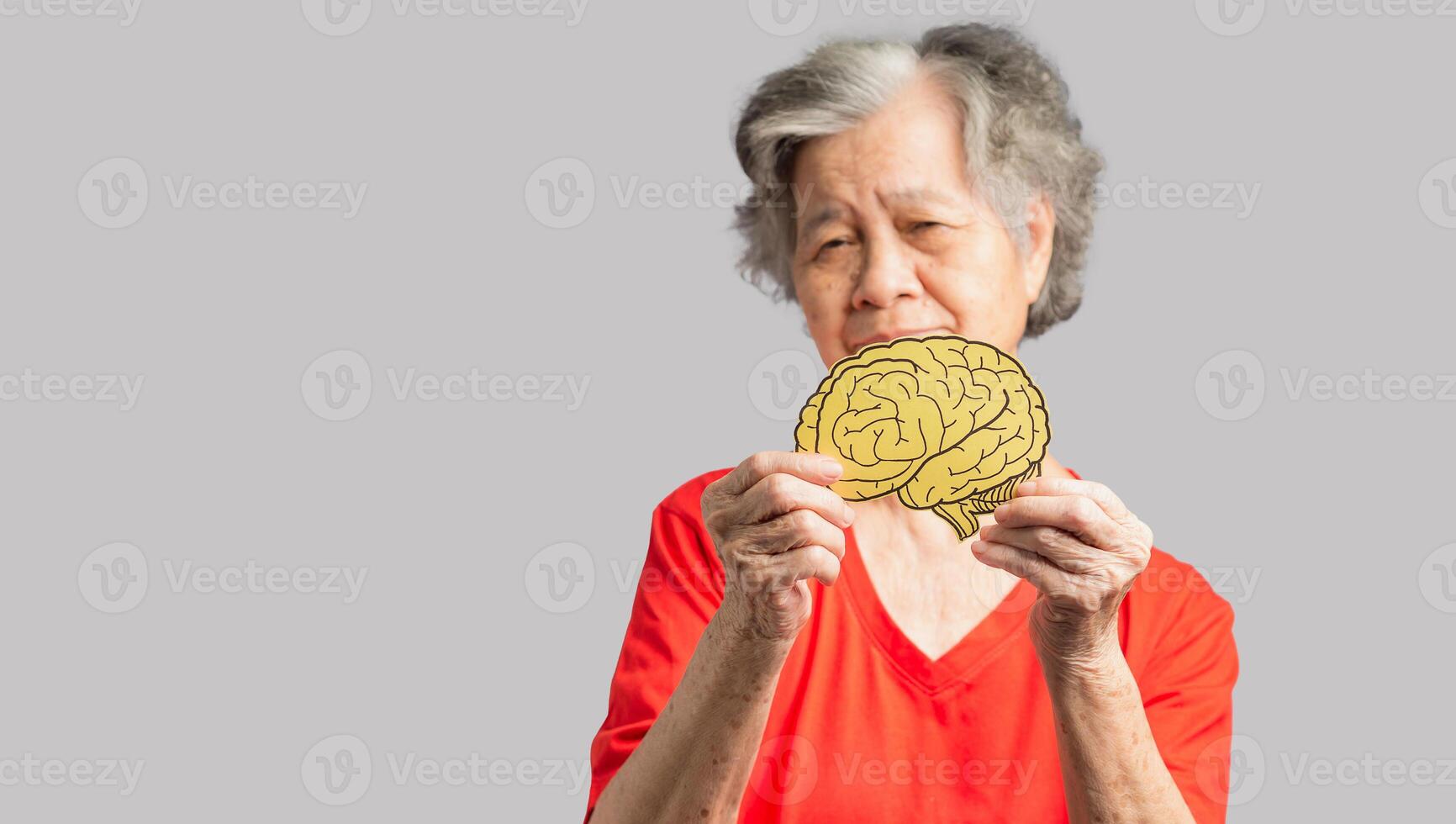 Portrait of a senior woman holding a brain shape made from yellow paper against a gray background photo