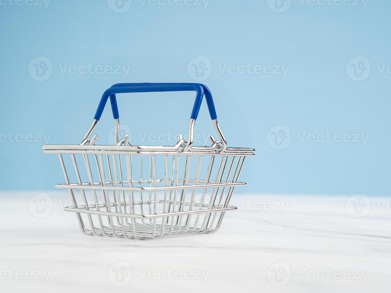 An empty mini shopping cart over a marble floor with a light blue background photo