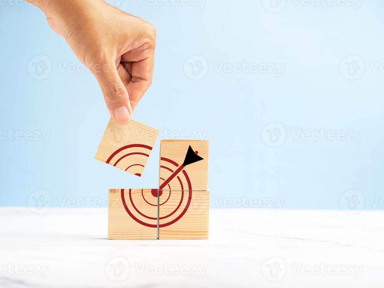 Close-up of hand holding a wooden cube with a target icon over a marble floor against a blue background photo