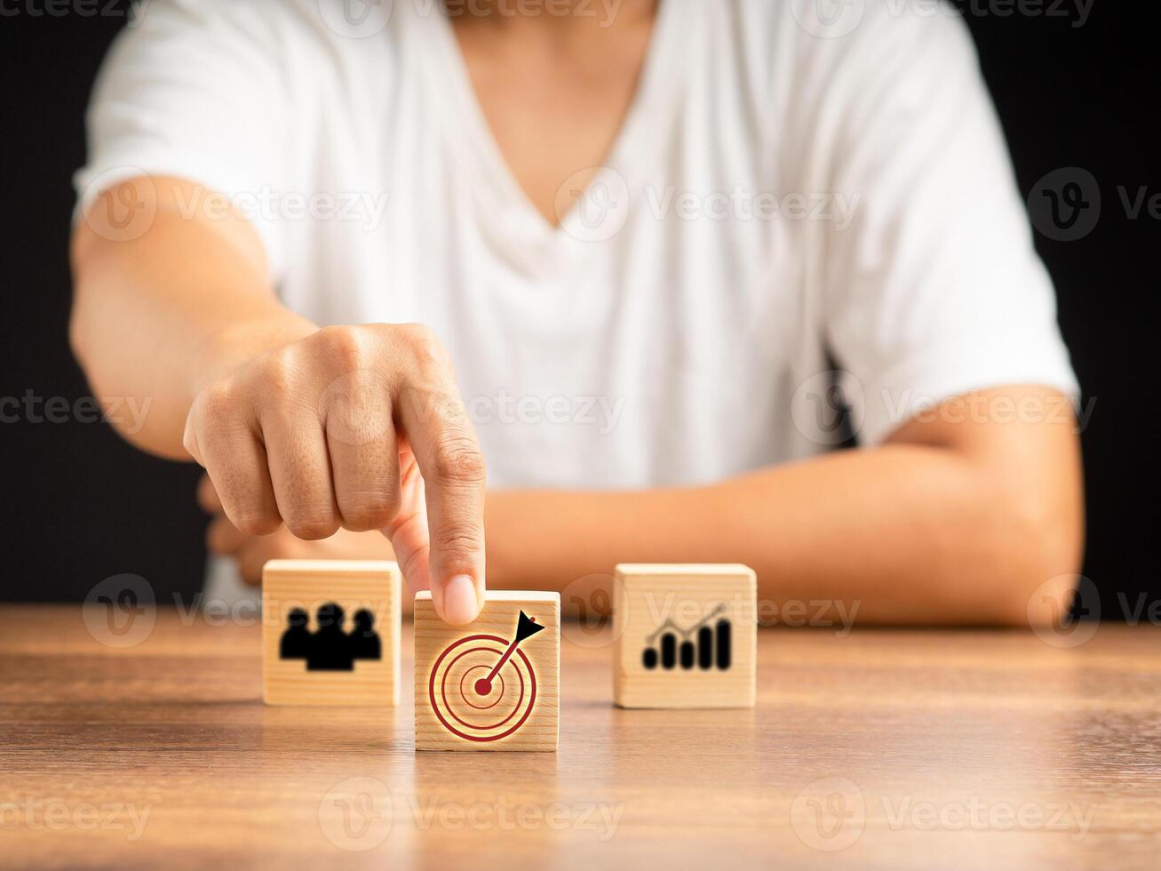 Young man holding a wooden cube with business icons arranged on the table while sitting in the office photo