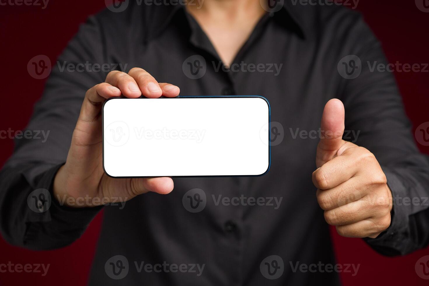 Hand holding a horizontal mobile phone with a blank white screen and showing thumbs up while standing on a red background photo