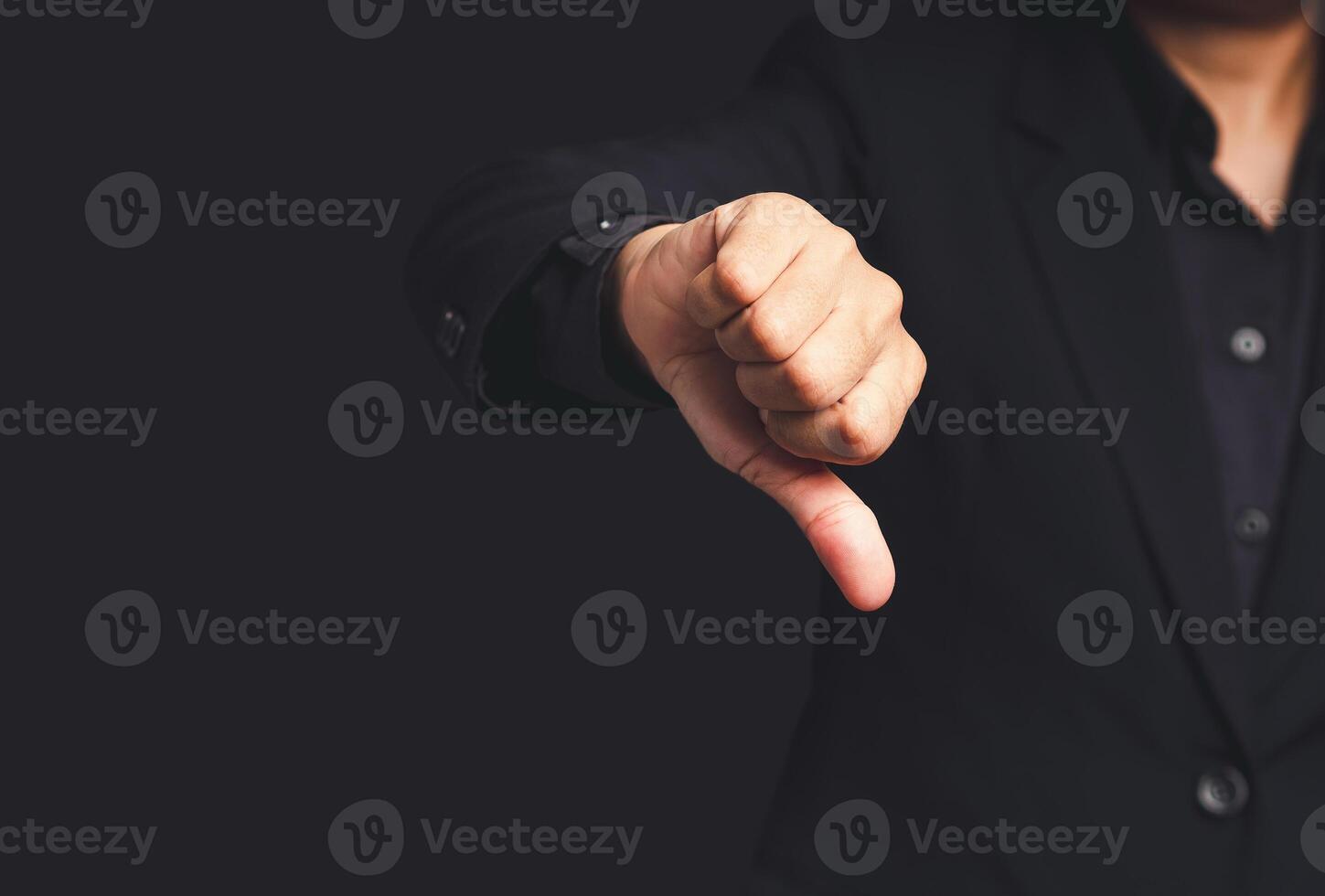 Close-up of businessman hand in a black suit showing thumbs down while standing on a gray background photo