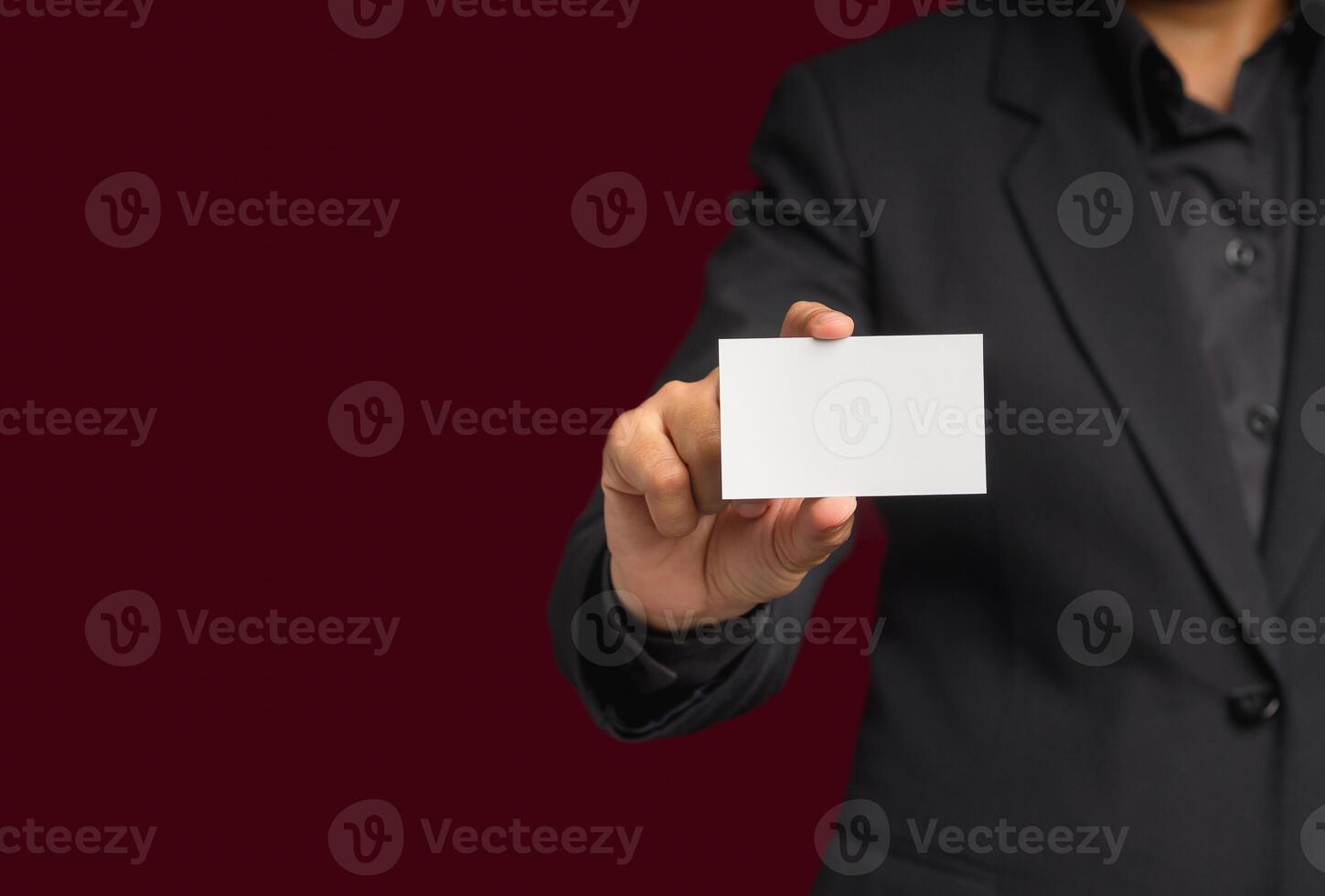 Businessman in a suit holding a name card mockup while standing over red background photo