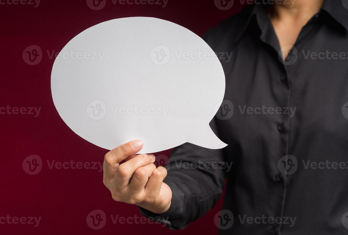 Text speech bubble concept. Close-up of hand holding a white speech bubble against a red background photo