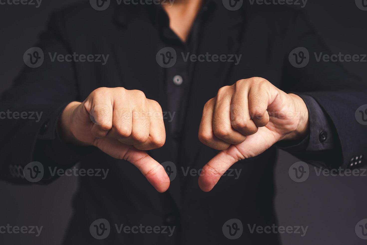 Negative concept. Close-up of businessman hands in a black suit showing thumbs down while standing on a gray background photo