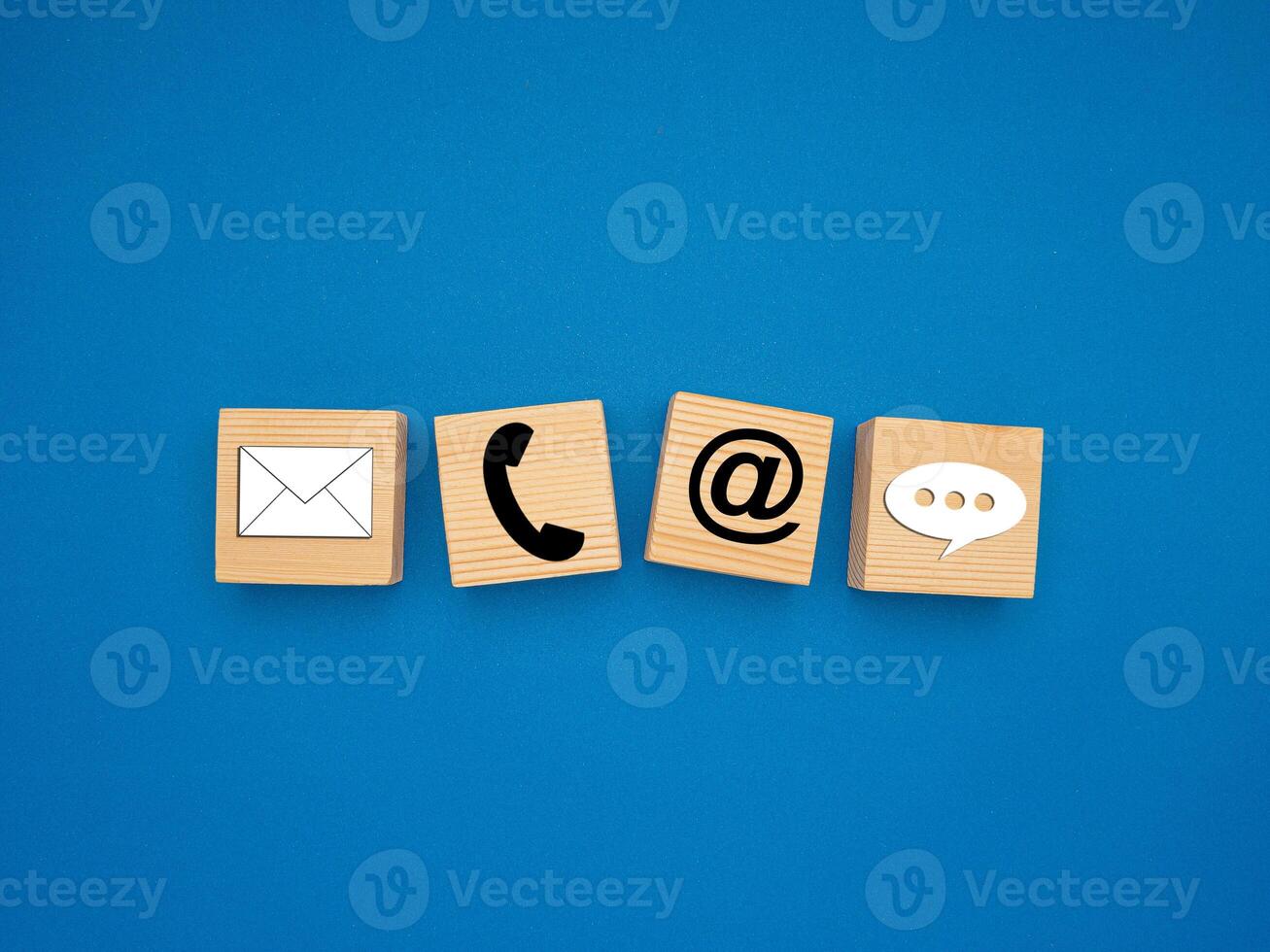 Wooden cubes with symbols of telephone, email, and speech bubble over a blue background photo