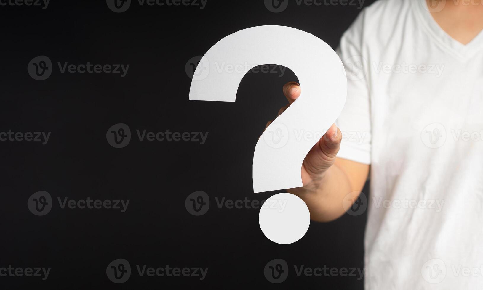 Hand holding a white question mark paper while standing on a gray background photo