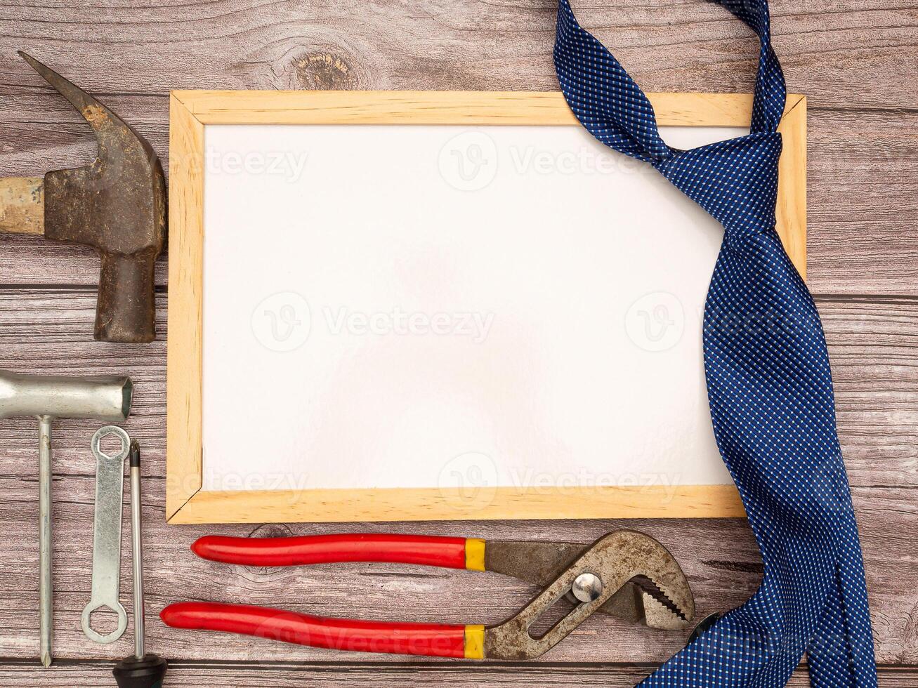 Happy Father's Day. A blank mini whiteboard, necktie, construction tools, a hammer, screwdriver, screws, and pliers are on a wooden table photo