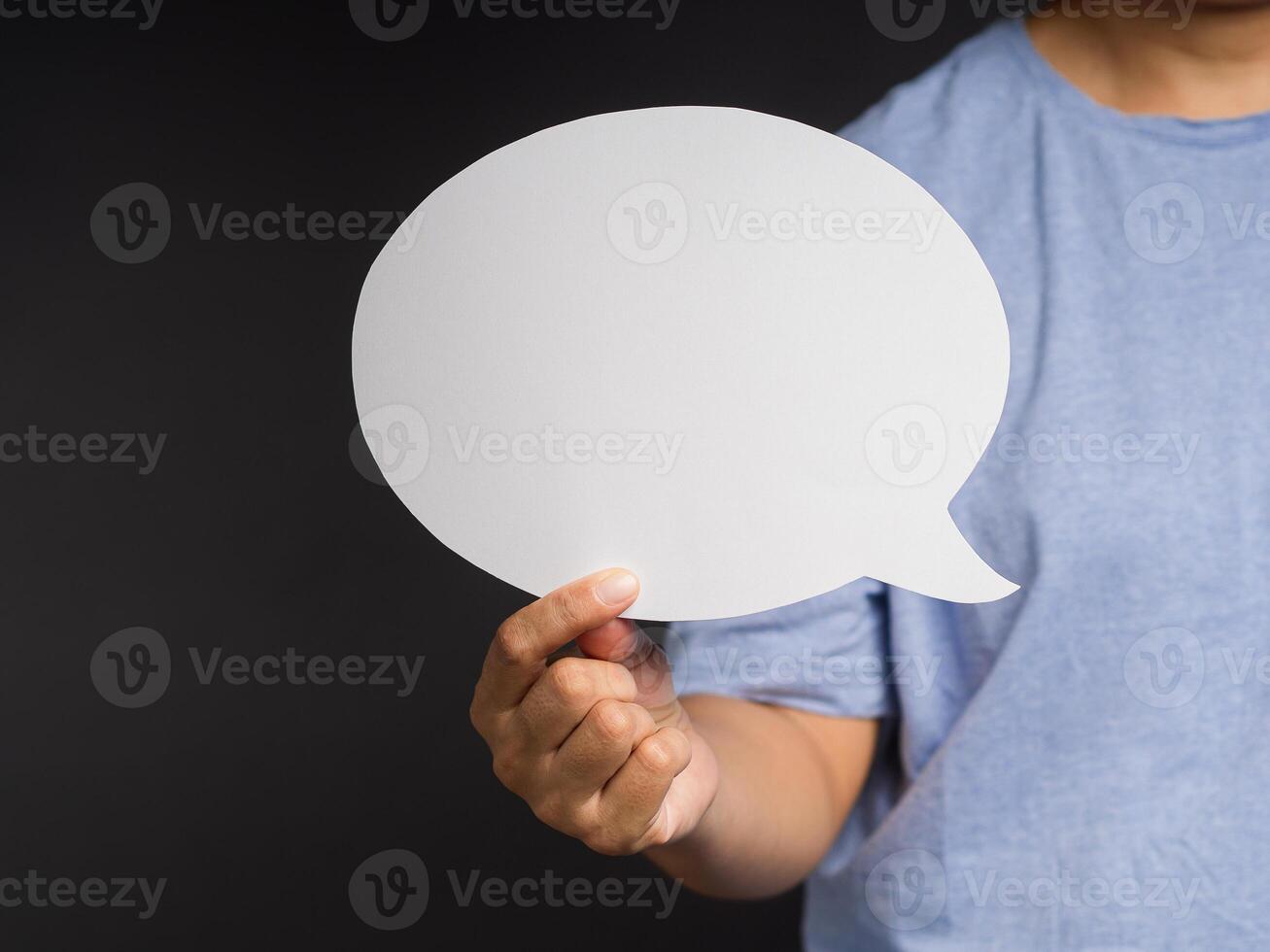 Hand holding a white speech bubble against a gray background while standing in the studio photo