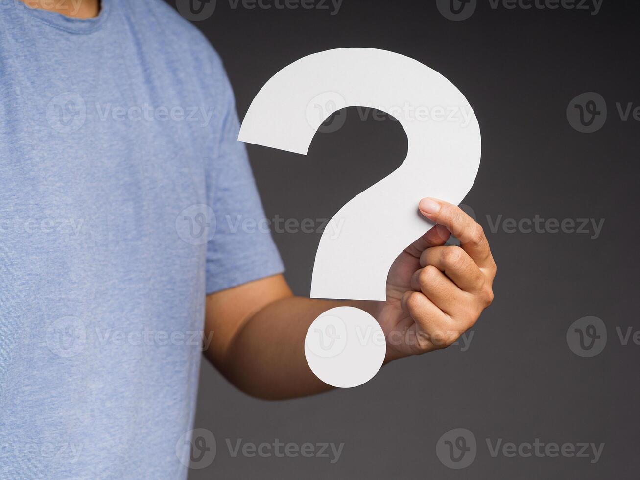 Hand holding a white question mark paper while standing on a gray background photo