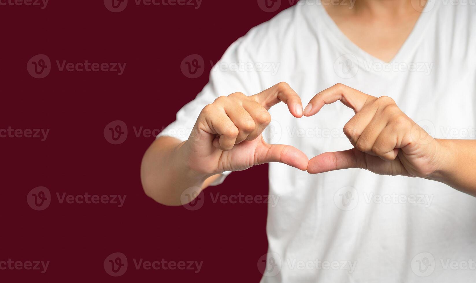 Man in white casual making heart figure love sign with fingers while standing on a red background photo