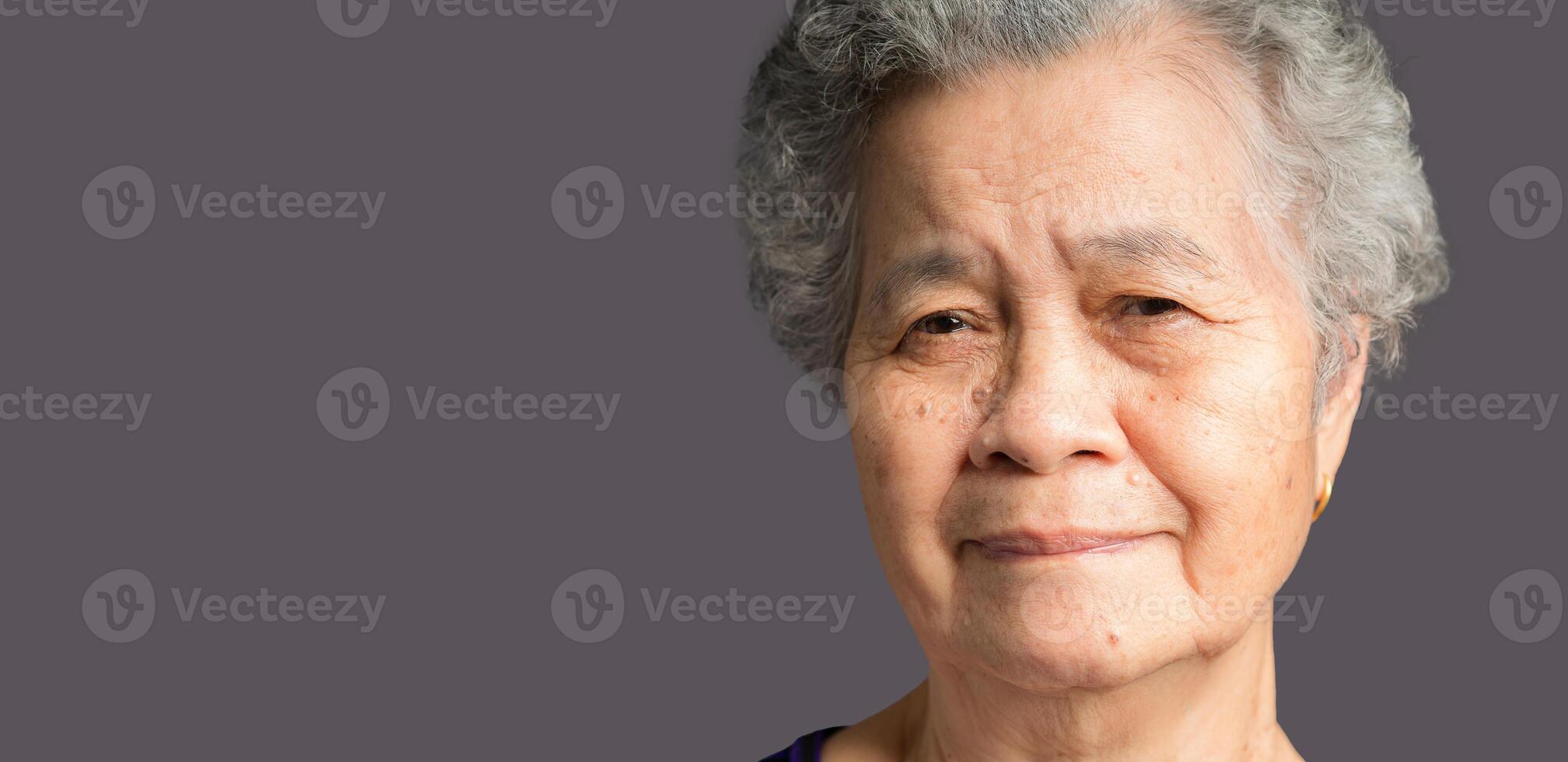 Senior woman with short gray hair looking at the camera with a smile while standing on gray background photo